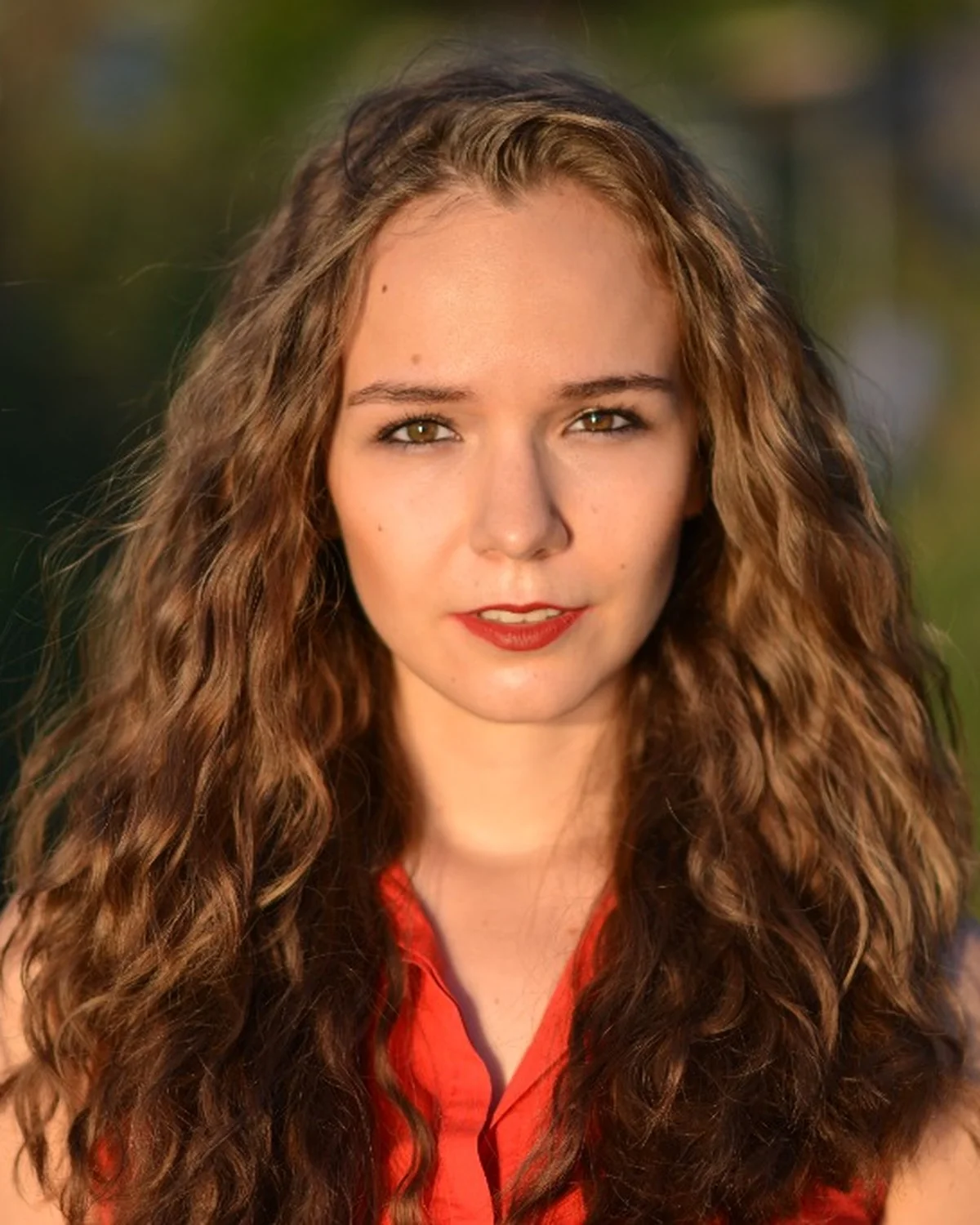 Golden Hour Nahaufnahme Porträt junger Frau mit Locken und rotem Kleid